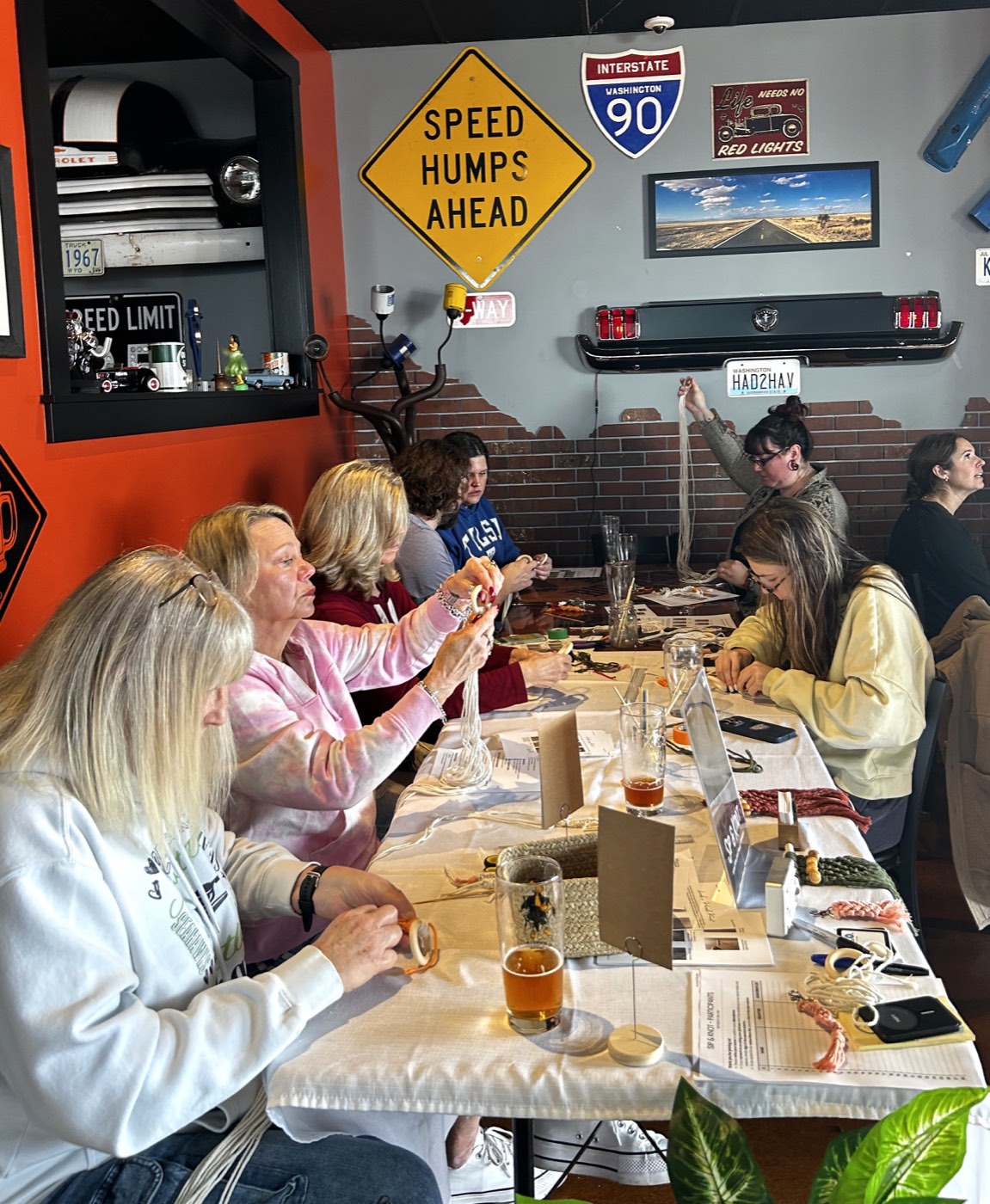A packed table of workshop guests knotting rope together at Big Block Brewery, surrounded by vintage highway signs