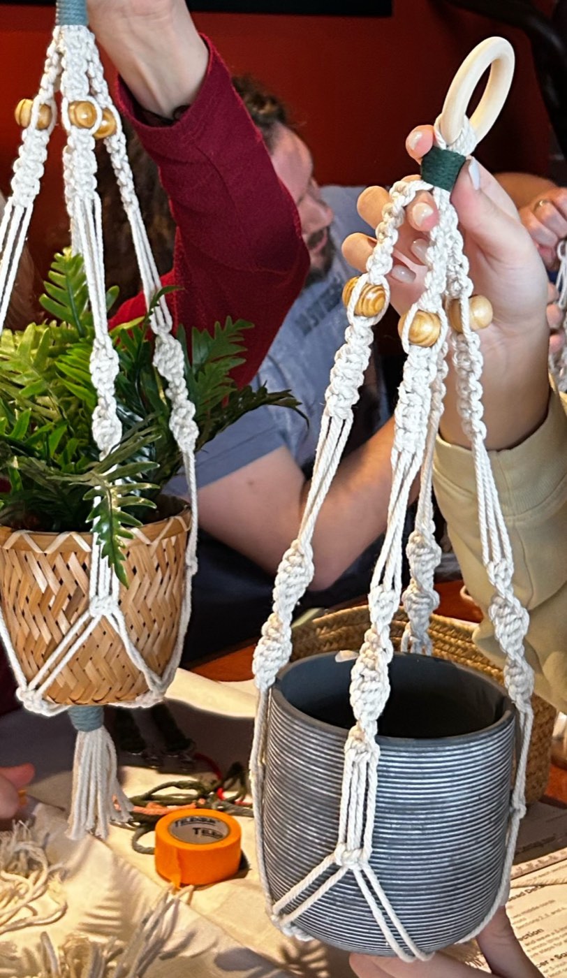 Two finished macramé plant hangers with wooden beads, held up mid-workshop