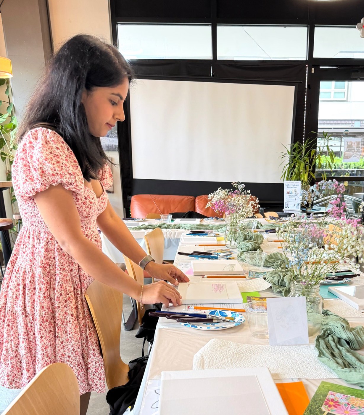 Arunima arranging a long workshop table with fresh flowers, rope, and craft supplies