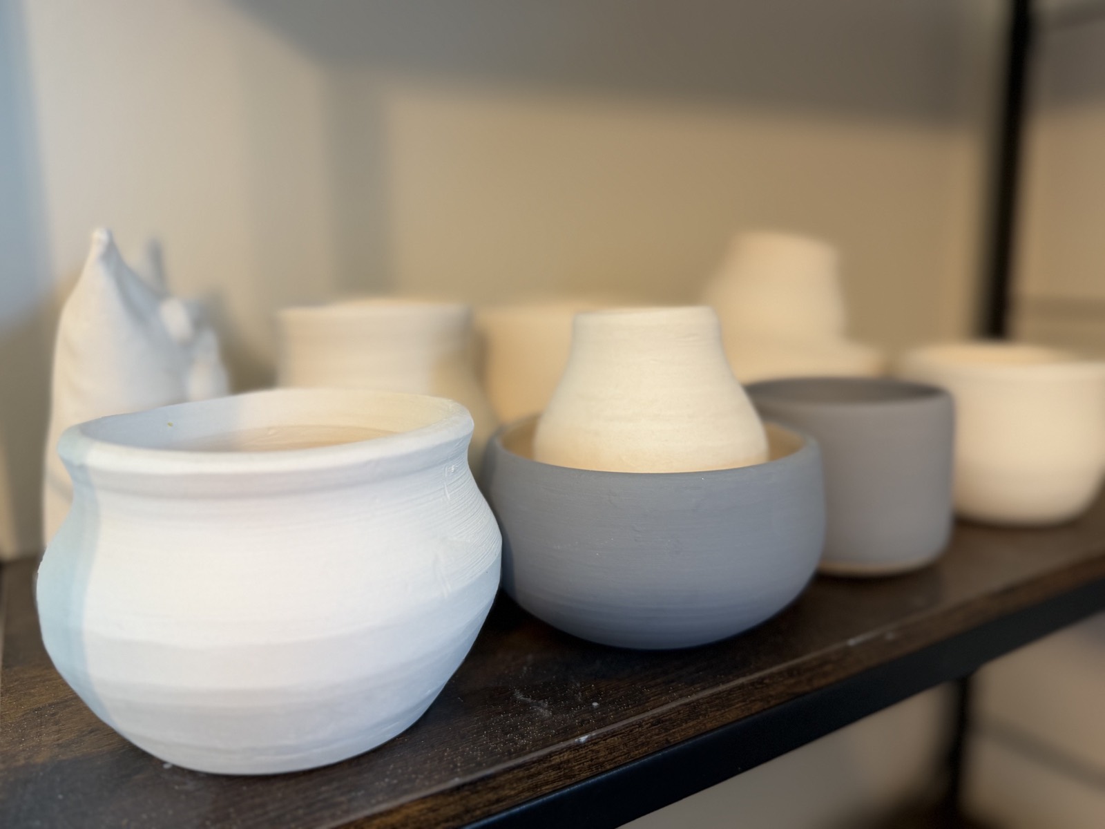 Rows of bisque-fired bowls and cups made by studio members, waiting on a shelf