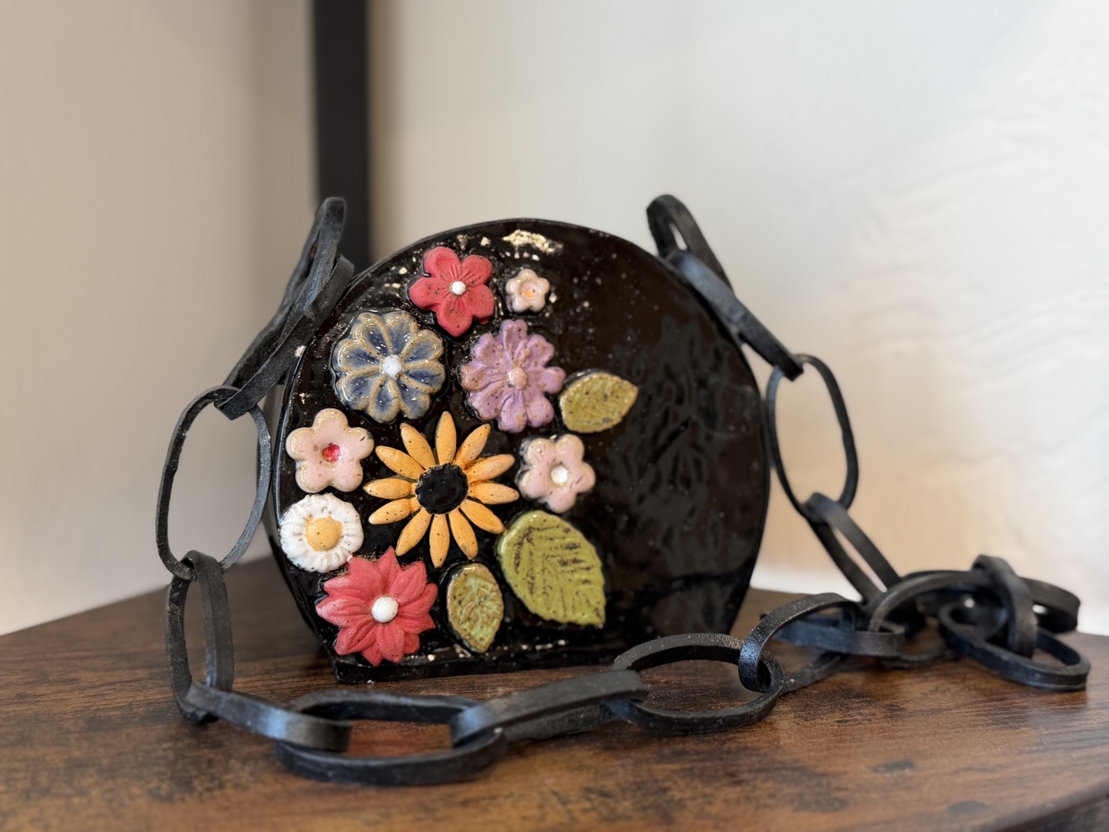 A ceramic purse with hand-formed clay flowers and a wrought-iron-look chain strap, the links feeling like real metal