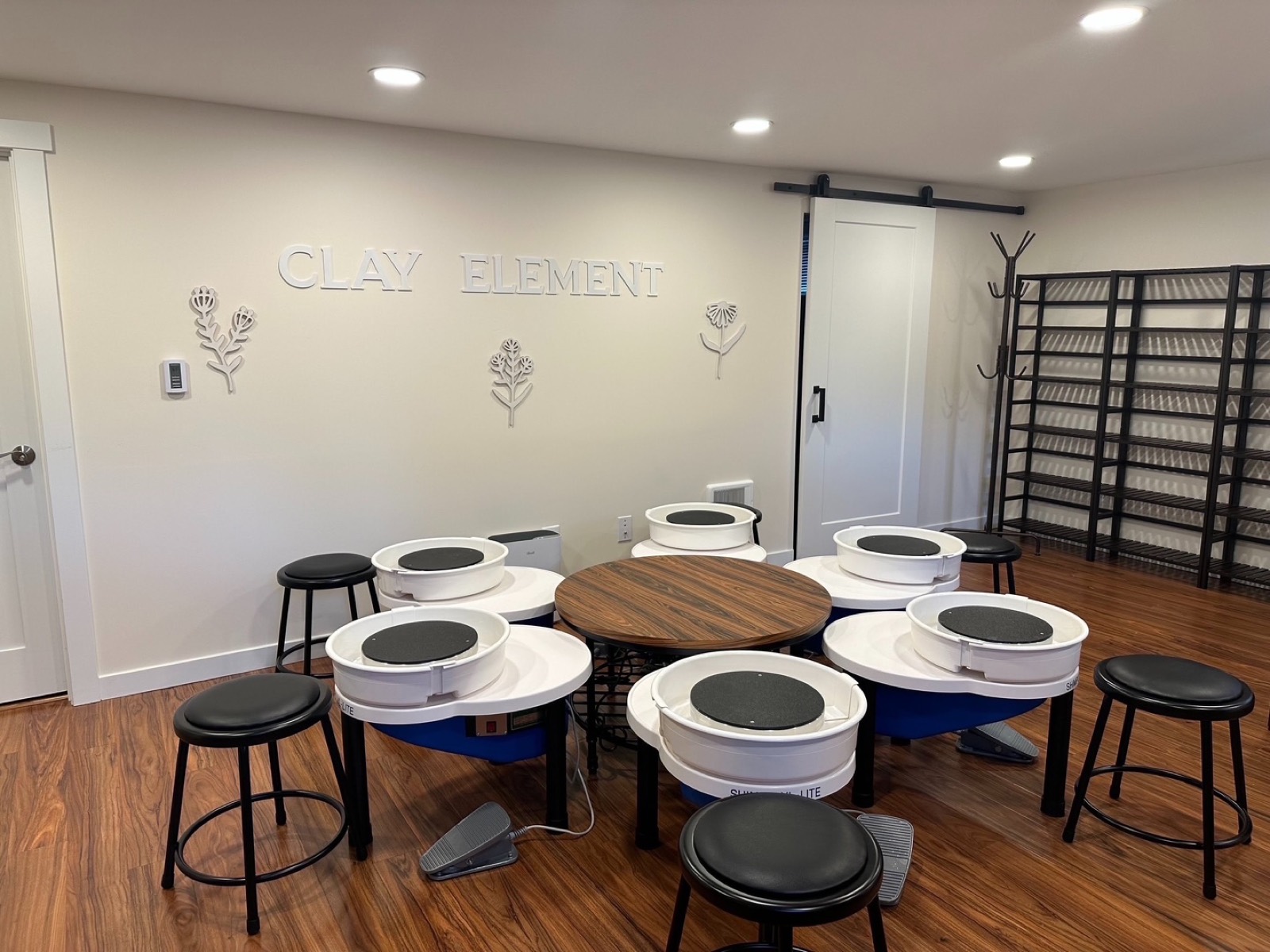The Earth room at Clay Element, a circle of pottery wheels and stools beneath the studio's carved wall sign