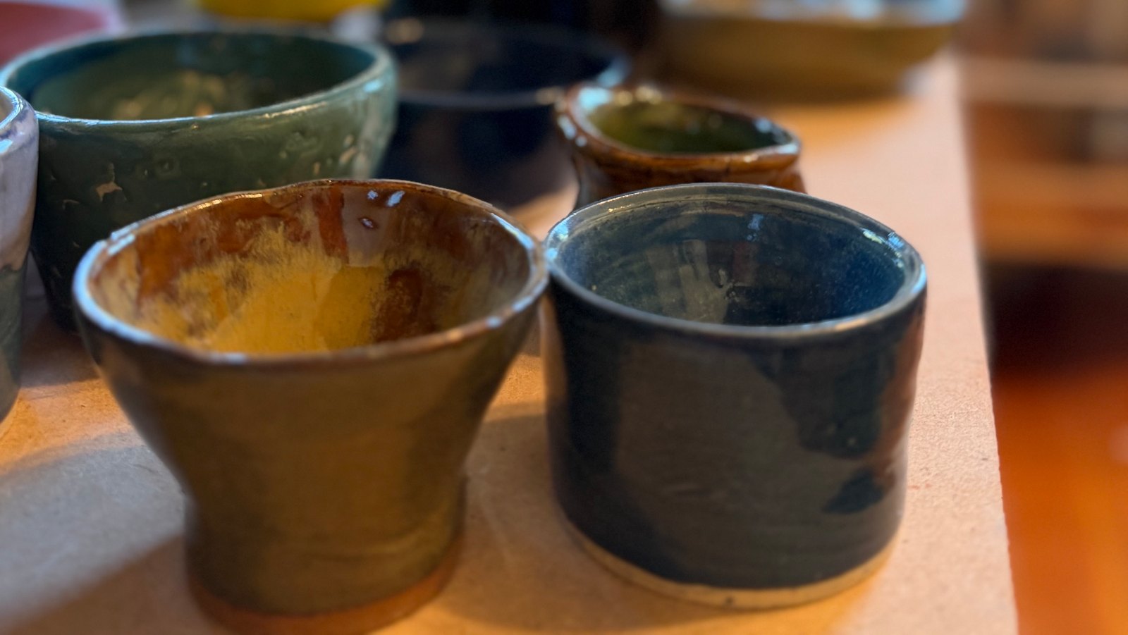 Small glazed cups and bowls fresh out of the kiln, cooling on a studio table