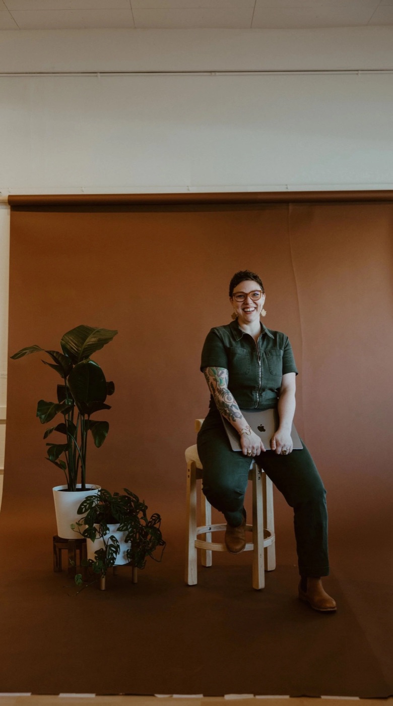 Sarah, founder of Making Local, sitting on a stool with a laptop against a warm terracotta backdrop
