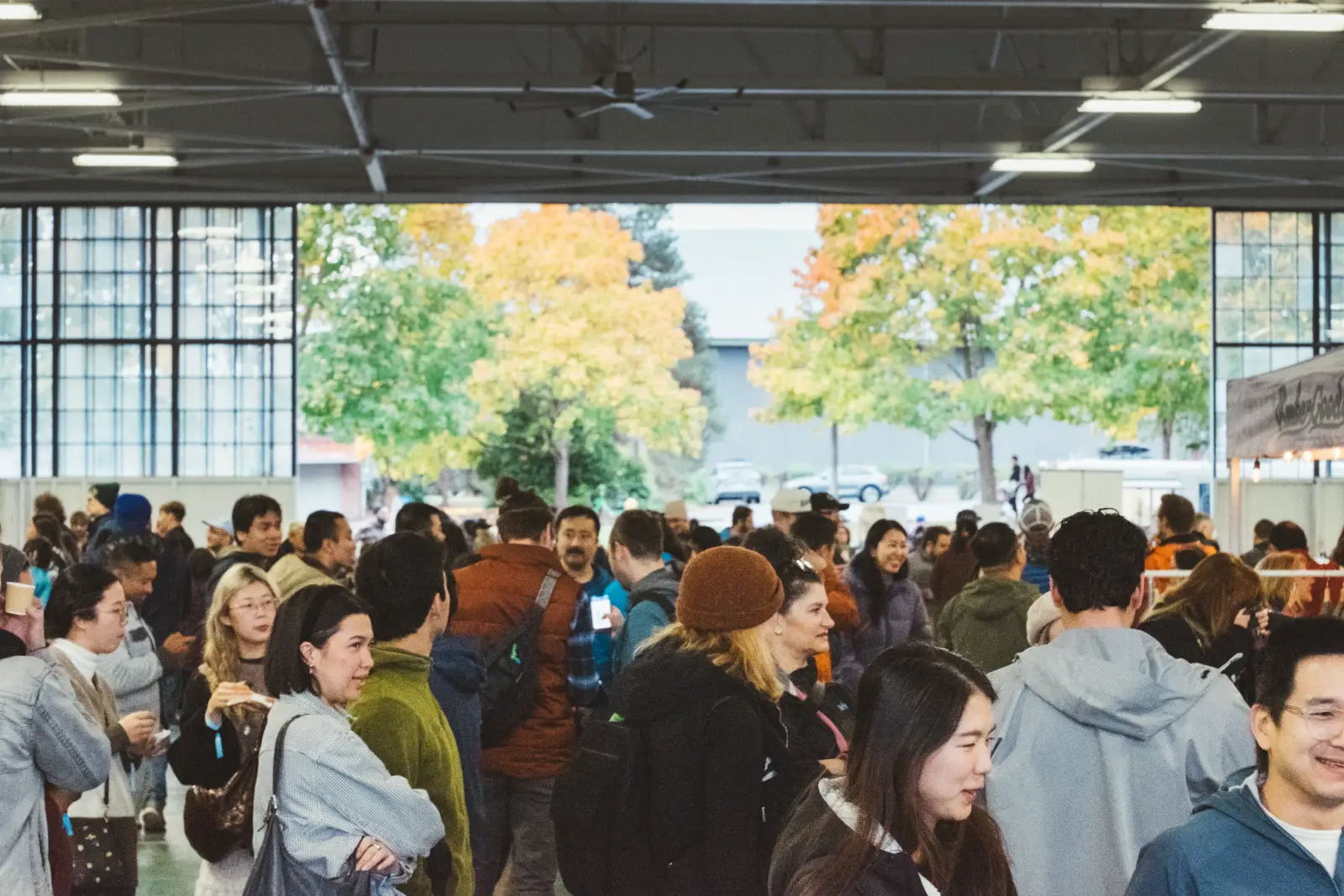 Crowds of festival-goers inside Hangar 30 with autumn trees through the open hangar door